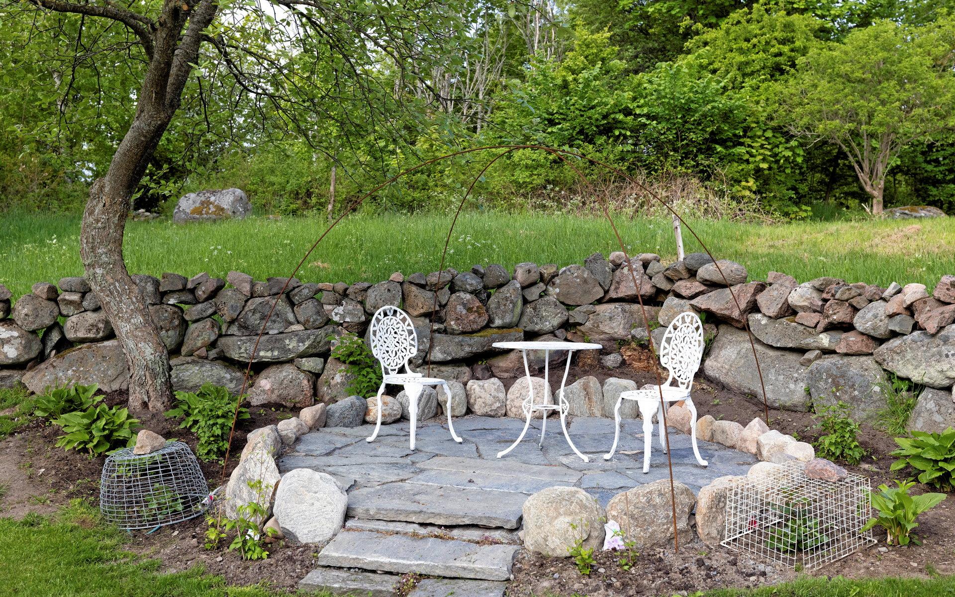 I trädgårdens bortre hörn går det att ta sig en paus på en altan under böjda armeringsjärn, där växter så småningom ska klättra.